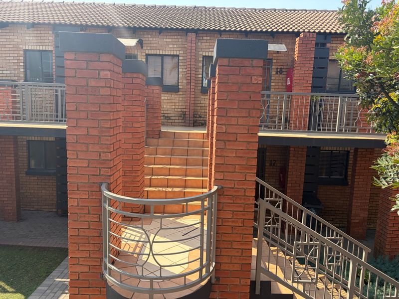 Exterior view of a face brick apartment complex featuring a tiled staircase, metal balustrades, and paved access paths.