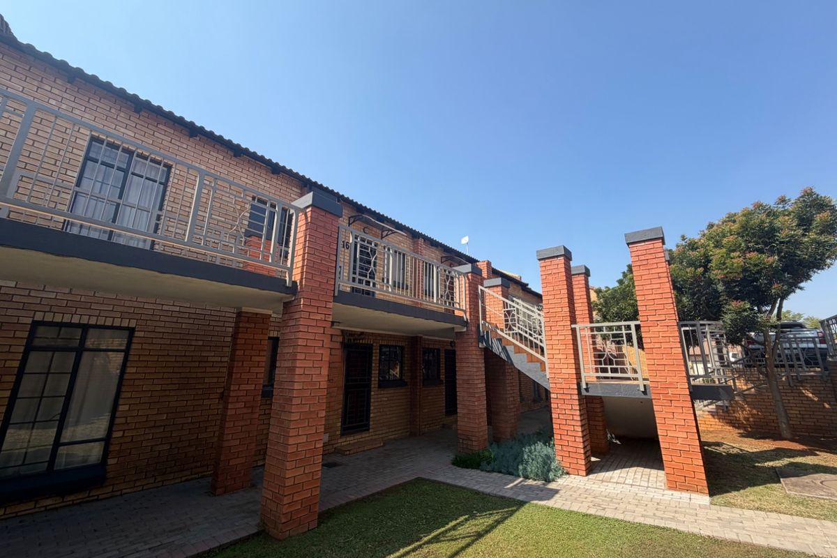 Rear view of a face brick apartment building featuring an external staircase, metal balustrades, and a well-maintained paved walkway with a small lawn area.