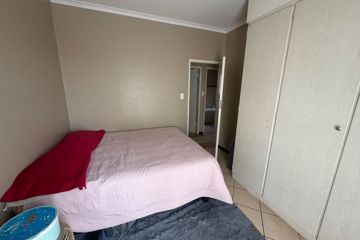 A bedroom featuring built-in cupboards, tiled flooring, and neutral wall tones, with direct access to an adjoining bathroom.