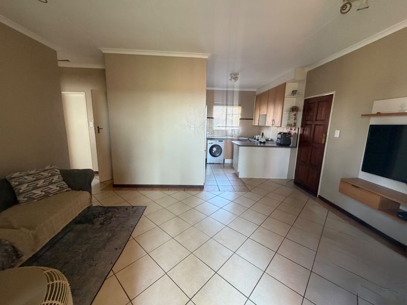 Open plan living area featuring tiled flooring and a functional kitchen with built-in cabinetry, integrated appliances, and direct access to the living space.