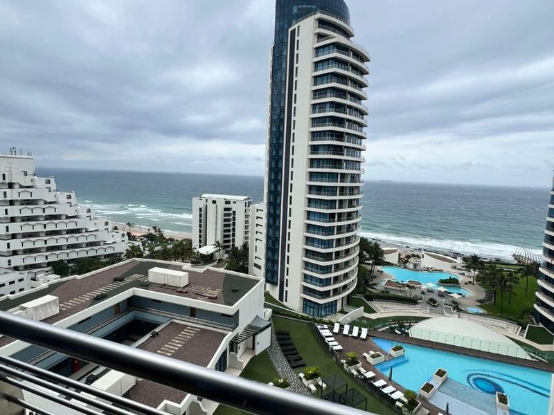Elevated coastal view overlooking the apartment complex, swimming pools, and the ocean horizon.