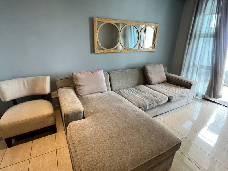 A well-lit living room featuring neutral tiled flooring, a feature wall, and large sliding glass doors providing access to the balcony.