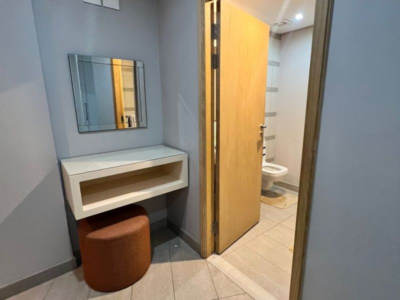 A bedroom area featuring a built-in vanity unit with a mirror, leading into an en-suite bathroom with tiled flooring and modern finishes.