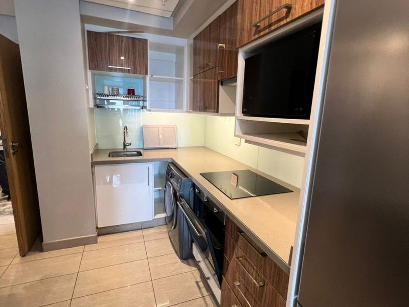 Modern galley-style kitchen featuring wood-grain and white cabinetry, stone countertops, integrated appliances, and sleek tiled flooring.