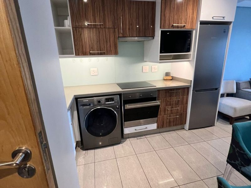 Modern kitchen featuring wood-grain cabinetry, stone countertops, glass splashback, and integrated appliances including an oven, hob, and fridge-freezer.
