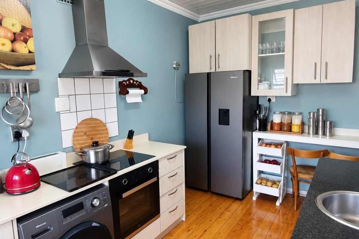 A functional kitchen featuring timber flooring, light-toned cabinetry, a stainless steel extractor fan, built-in oven, and a tiled splashback.