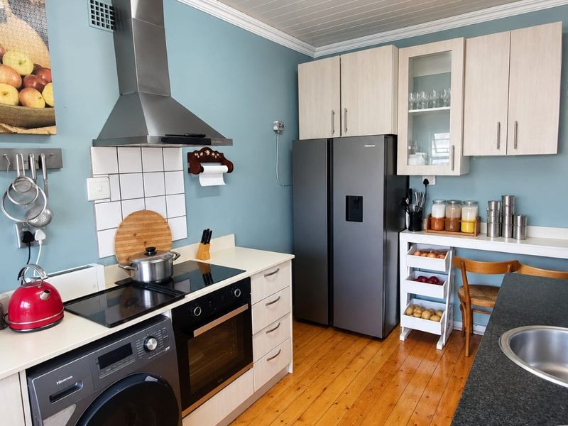 A functional kitchen featuring timber flooring, light-toned cabinetry, a stainless steel extractor fan, built-in oven, and a tiled splashback.