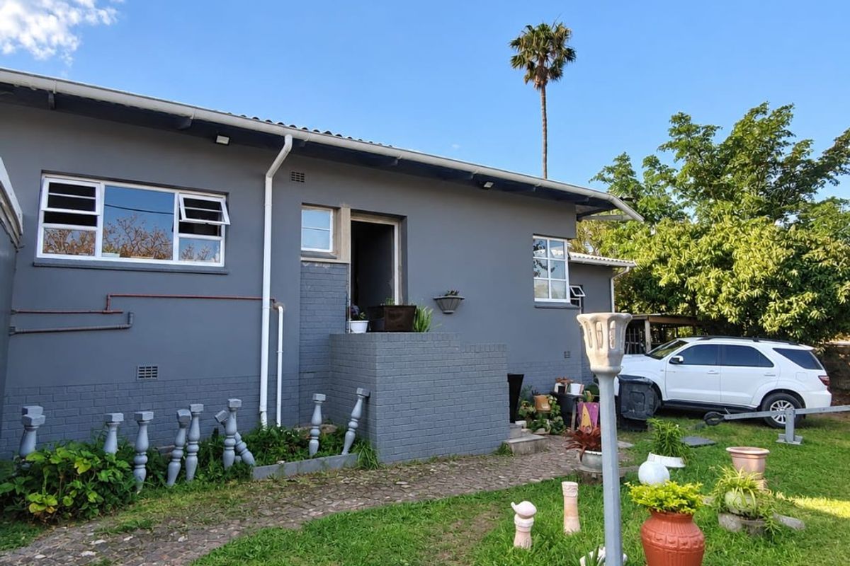 Rear view of the property featuring a grey painted brick facade, paved garden path, and established lawn area.
