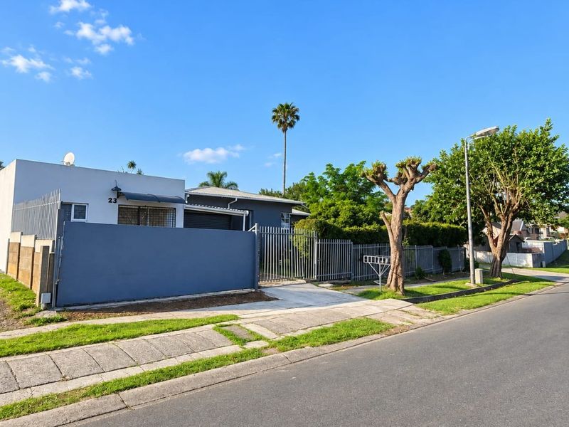 Front exterior view of a residential property featuring a solid boundary wall, metal fencing, and a paved driveway entrance.
