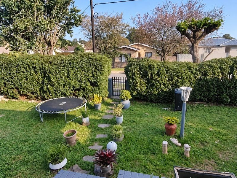 A private residential garden featuring a stone pathway, manicured hedges, and a brick retaining wall, providing a pleasant outdoor space.