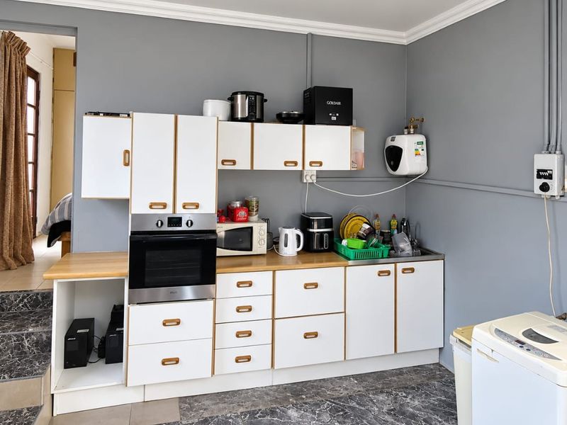A functional kitchen area featuring white cabinetry, built-in oven, laminate countertops, and tiled flooring with visible wall-mounted electrical conduits.