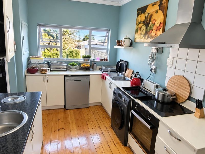 A functional kitchen featuring timber flooring, built-in cabinetry, a stainless steel extractor fan, electric hob, and a double sink with a view.