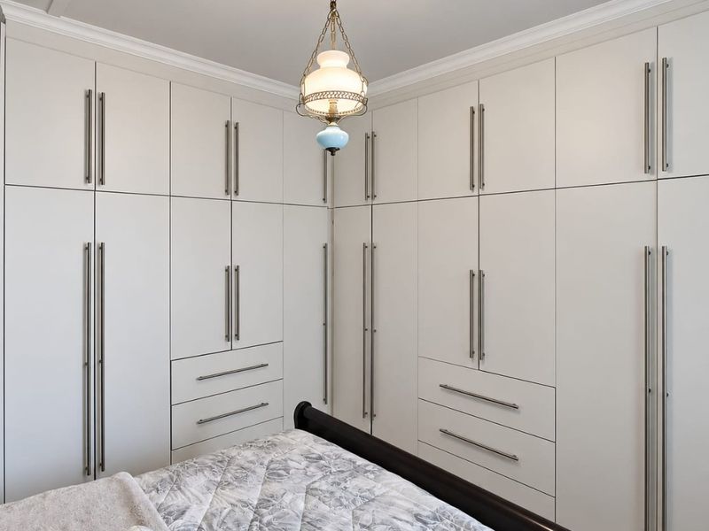 A well-appointed bedroom featuring extensive floor-to-ceiling built-in cabinetry with integrated drawers and modern brushed metal hardware.