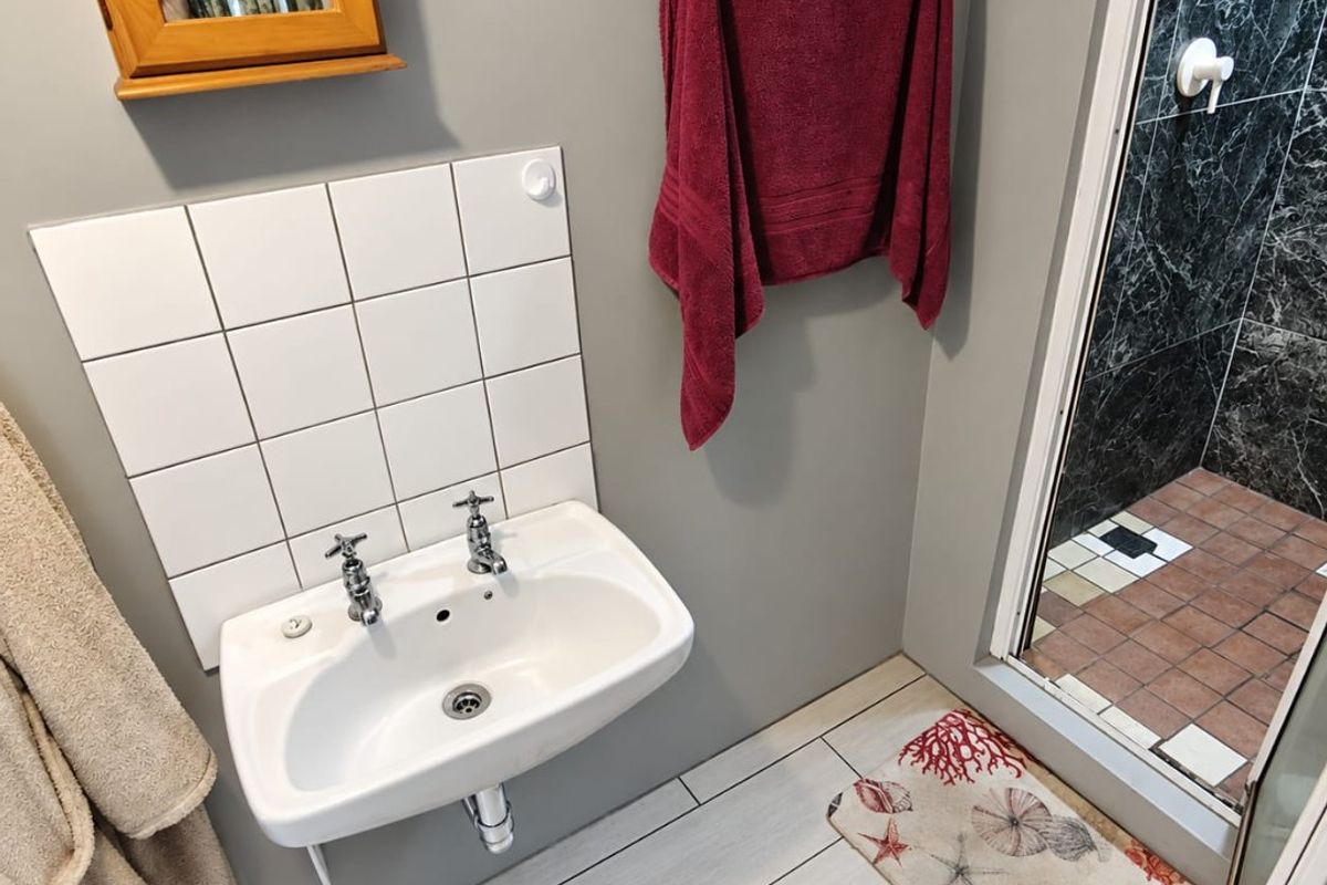 A functional bathroom featuring a wall-mounted basin with tiled splashback and a separate shower enclosure with marble-effect wall tiling.