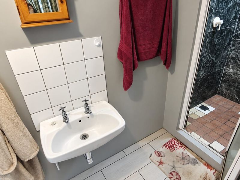 A functional bathroom featuring a wall-mounted basin with tiled splashback and a separate shower enclosure with marble-effect wall tiling.