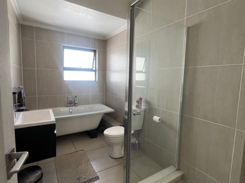 A modern bathroom featuring a freestanding bathtub, a separate glass-enclosed shower, a vanity cabinet, and neutral floor-to-ceiling wall tiling.