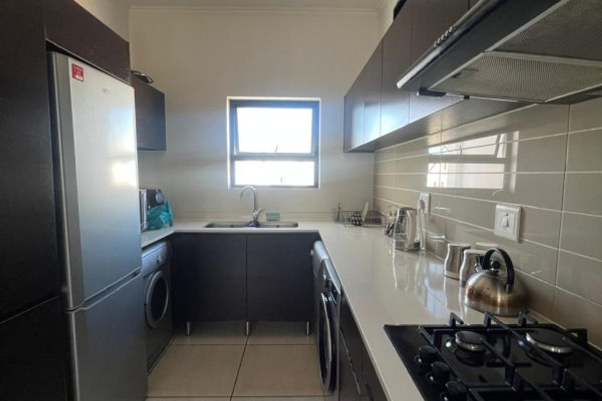 A modern galley-style kitchen featuring dark cabinetry, stone countertops, a gas hob with extractor fan, and tiled flooring.