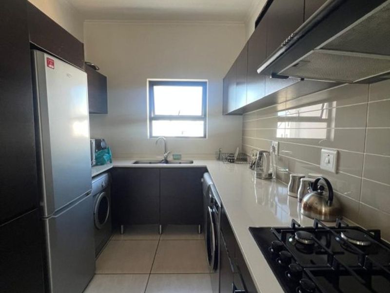 A modern galley-style kitchen featuring dark cabinetry, stone countertops, a gas hob with extractor fan, and tiled flooring.