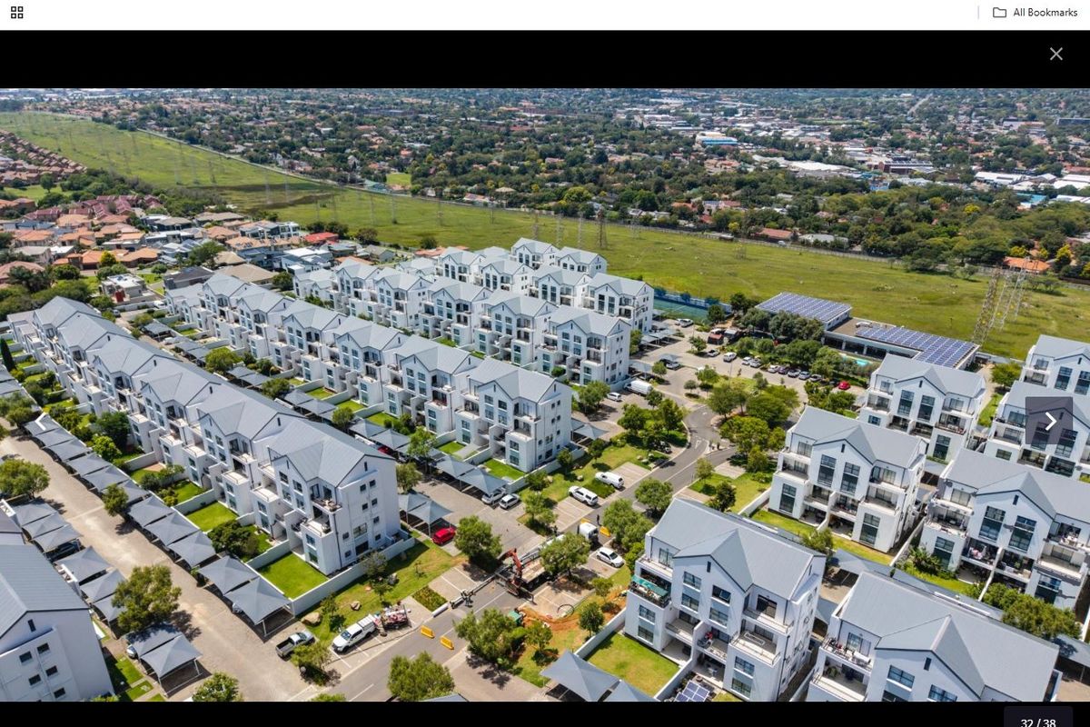 Aerial view of a modern residential apartment complex featuring multiple blocks, paved driveways, carports, and landscaped communal garden areas.