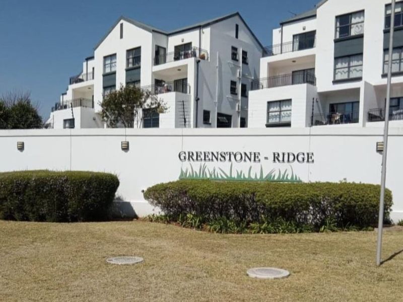Exterior view of the Greenstone Ridge apartment complex featuring white facade architecture, balconies, and a secure boundary wall with electric fencing.