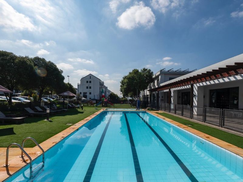 A well-maintained outdoor swimming pool area featuring a lap pool, artificial grass surround, and a covered pergola structure.