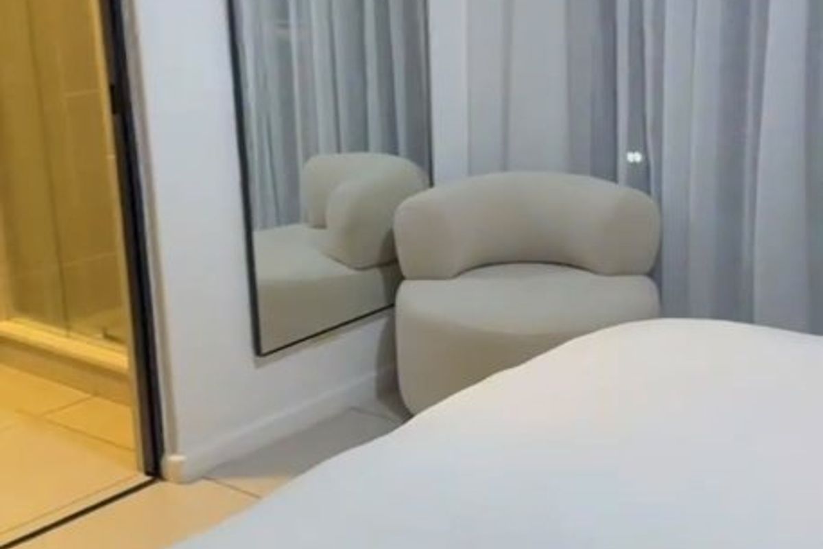 A modern bedroom featuring tiled flooring, sheer curtains, and an adjoining en-suite bathroom with a glass-enclosed shower.