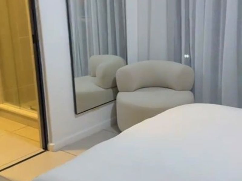 A modern bedroom featuring tiled flooring, sheer curtains, and an adjoining en-suite bathroom with a glass-enclosed shower.