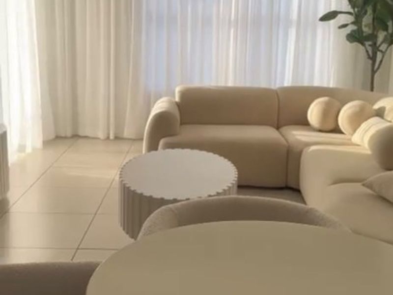 Bright open-plan living area featuring large format floor tiles and floor-to-ceiling window treatments, creating a light and airy atmosphere.