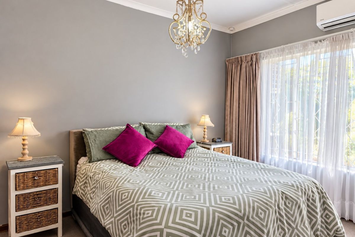 A well-maintained bedroom featuring neutral wall tones, a split-system air conditioner, and a window fitted with security bars.