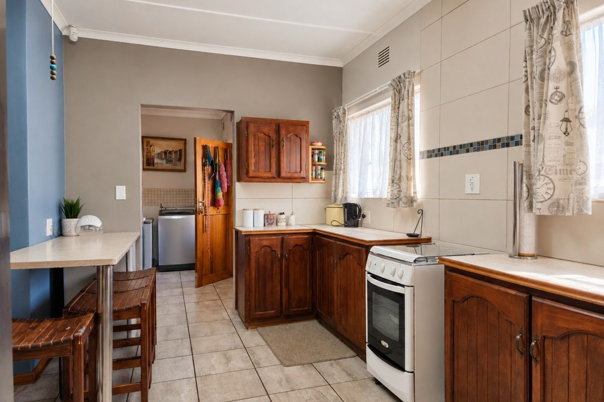 A functional kitchen featuring wooden cabinetry, tiled flooring, a tiled backsplash, and a breakfast bar, with an adjacent utility area visible through the doorway.