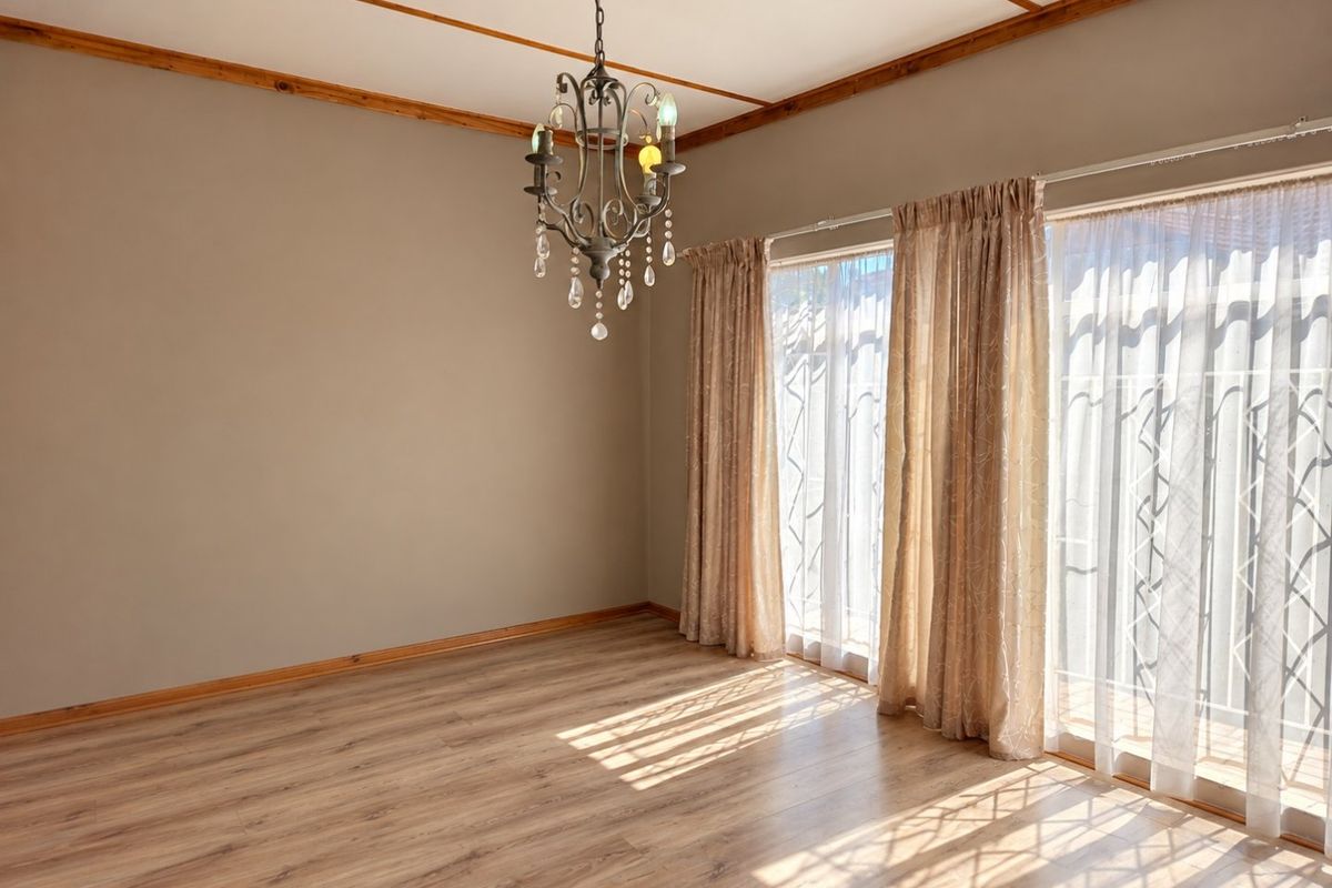 An empty living room featuring laminate flooring, timber ceiling beams, a decorative chandelier, and large sliding glass doors providing natural light.