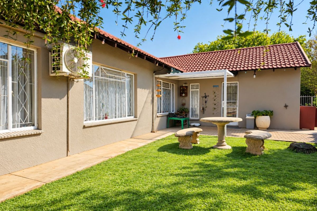 A well-maintained rear exterior view featuring a paved patio area, a neat lawn, and a tiled roof structure with an external air conditioning unit.