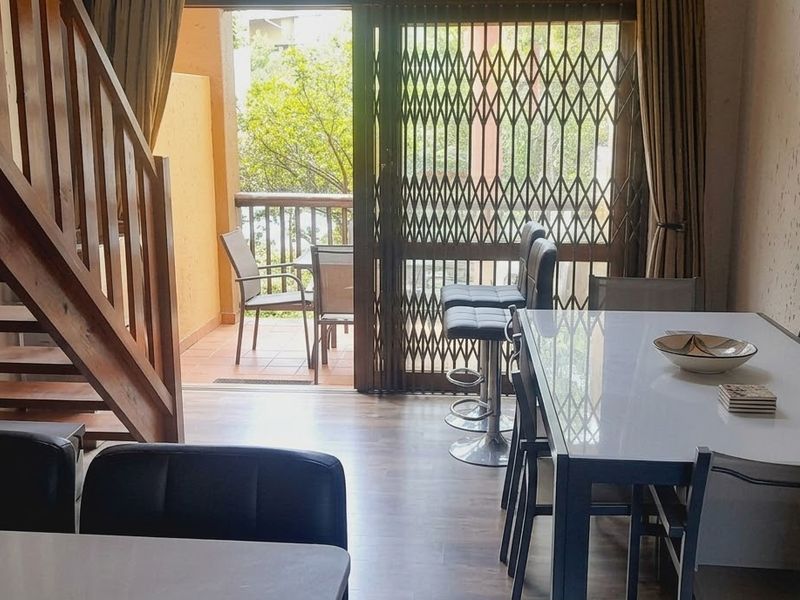 Open-plan living and dining area featuring a wooden staircase, laminate flooring, and direct access to a private balcony through sliding glass doors.