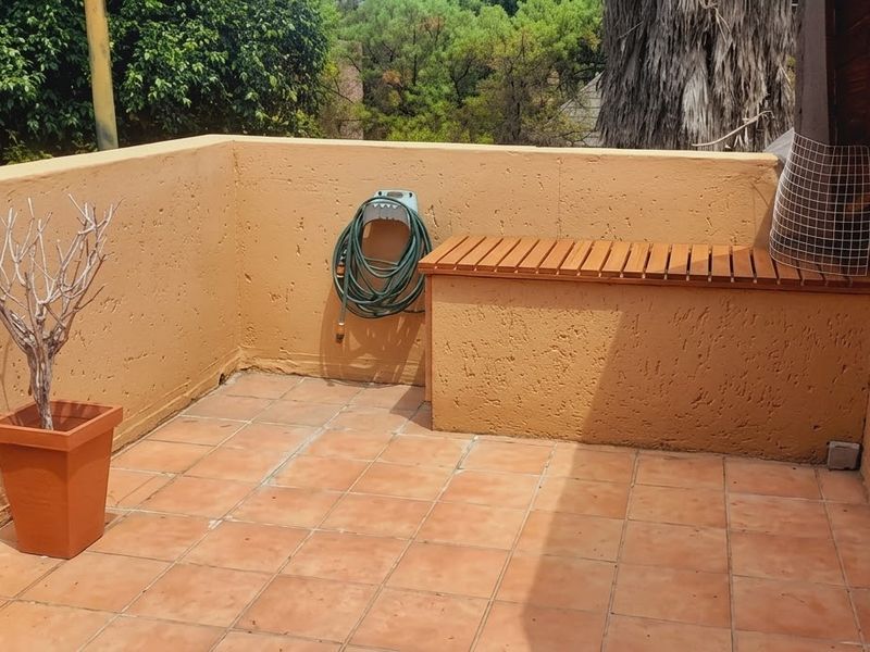 A private balcony featuring tiled flooring, a built-in masonry bench with a wooden seat, and a surrounding parapet wall.
