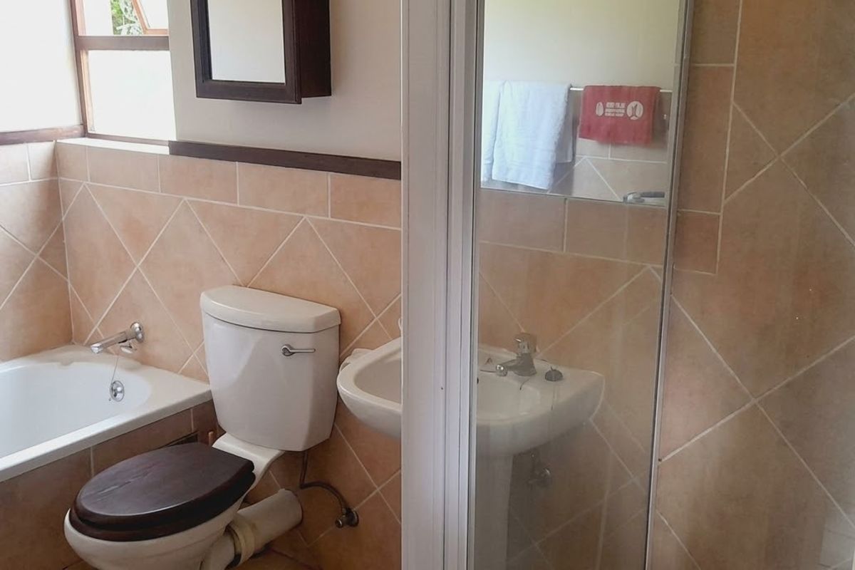 A functional bathroom featuring a bathtub, pedestal basin, and separate shower enclosure with neutral wall tiling.