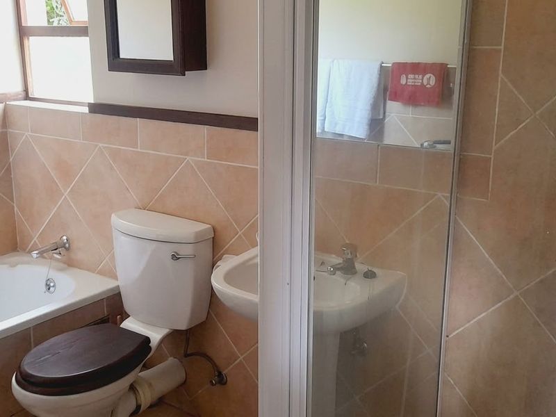A functional bathroom featuring a bathtub, pedestal basin, and separate shower enclosure with neutral wall tiling.