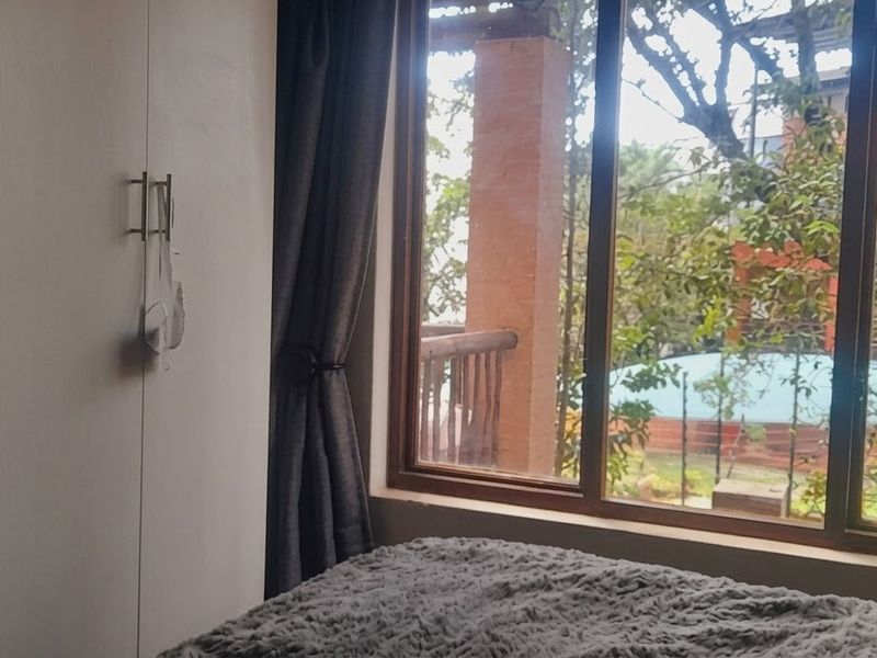 A bedroom featuring a built-in wardrobe and a large window providing natural light and a view of the surrounding greenery.