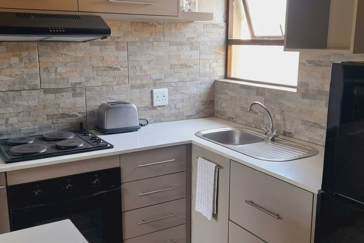 A compact, functional kitchen featuring modern cabinetry, stone-look tile backsplash, integrated electric hob, oven, and a stainless steel sink.