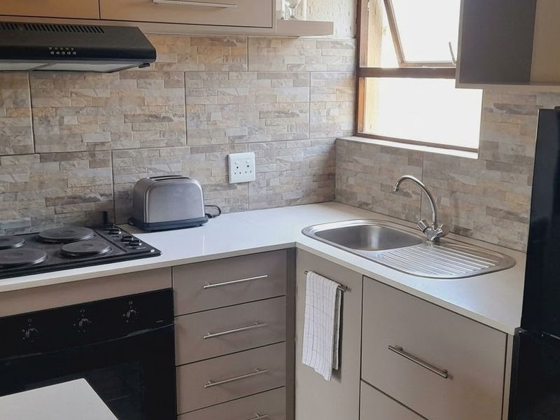 A compact, functional kitchen featuring modern cabinetry, stone-look tile backsplash, integrated electric hob, oven, and a stainless steel sink.