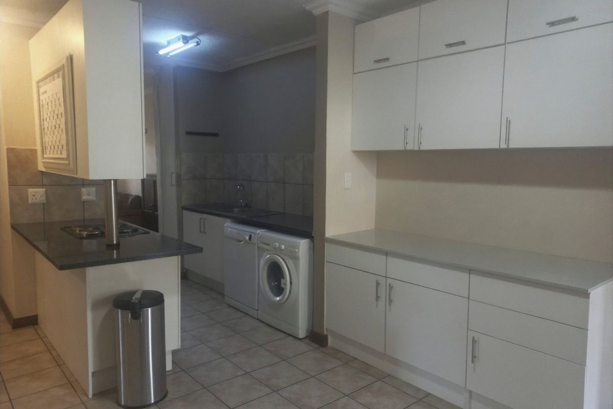 A functional kitchen featuring white built-in cabinetry, stone countertops, tiled backsplash, and tiled flooring with integrated laundry and cooking appliances.