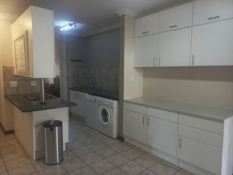 A functional kitchen featuring white built-in cabinetry, stone countertops, tiled backsplash, and tiled flooring with integrated laundry and cooking appliances.