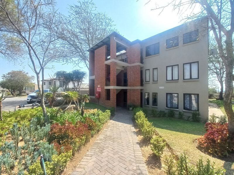 Exterior view of a multi-story apartment building featuring a brick facade, paved entrance walkway, and well-maintained landscaped garden area.