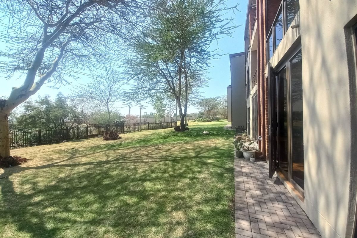 A view of the rear exterior featuring a paved walkway, a well-maintained lawn, and access to the apartment through large sliding glass doors.