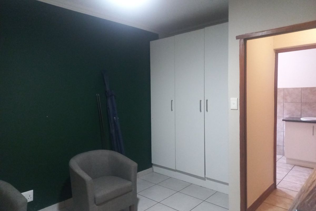 A bedroom featuring built-in cupboards, tiled flooring, and a dark accent wall, with an adjacent view into a tiled bathroom area.