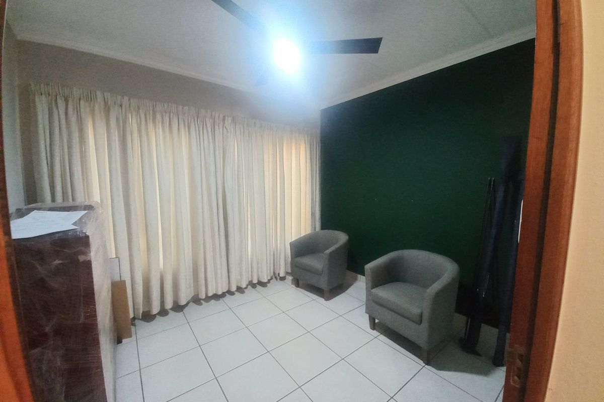 A living room featuring tiled flooring, a ceiling fan, and a dark green accent wall with floor-to-ceiling curtains.