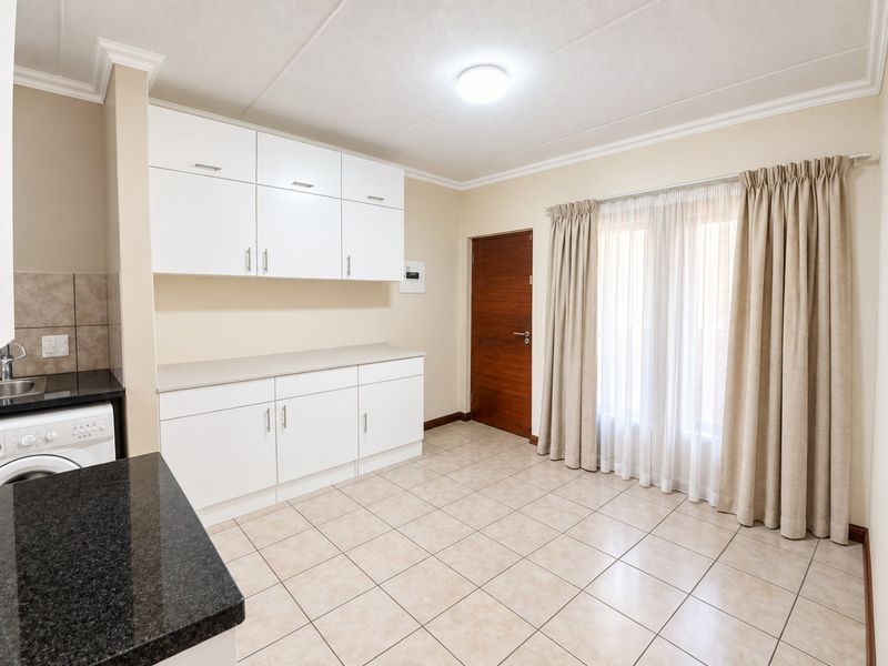 A clean, well-maintained kitchen featuring white built-in cabinetry, dark granite countertops, tiled flooring, and direct access to an adjacent room.