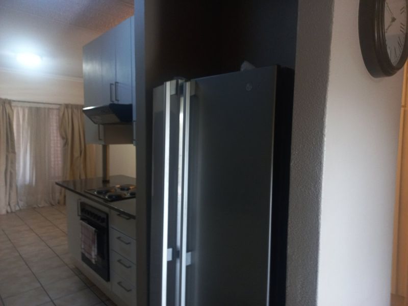 A functional kitchen area featuring built-in cabinetry, a hob, oven, and extractor fan, with tiled flooring and an adjacent living space.