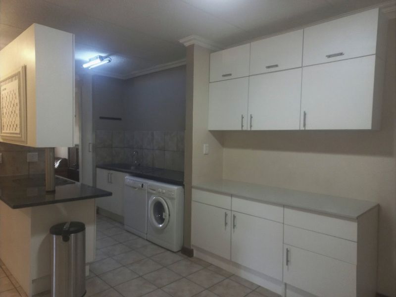 A functional kitchen featuring white built-in cabinetry, laminate countertops, tiled backsplash, and tiled flooring with integrated laundry appliance space.
