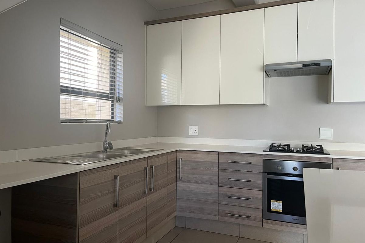 Modern kitchen featuring sleek two-tone cabinetry, stone countertops, integrated gas hob, built-in oven, and stainless steel sink with neutral tiled flooring.