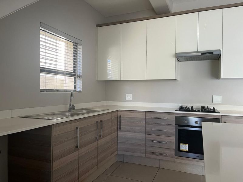 Modern kitchen featuring sleek two-tone cabinetry, stone countertops, integrated gas hob, built-in oven, and stainless steel sink with neutral tiled flooring.